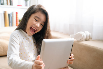 Asian  Cute child playing games with a tablet and smiling while sitting on sofa at home