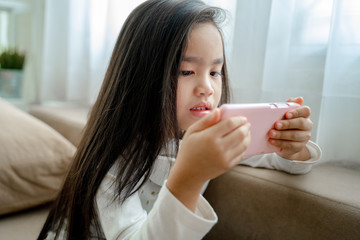 Cute child using a smartphone and smiling while sitting on sofa at home