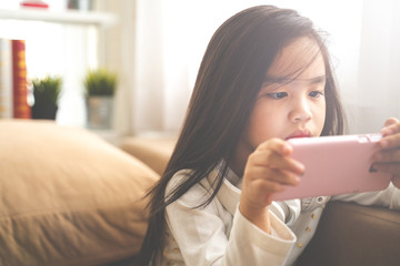 Cute child using a smartphone and smiling while sitting on sofa at home