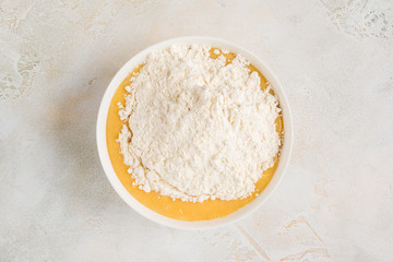 Dough cooking - flour adding in a white bowl with mix of sugar, eggs, cream and butter, top view