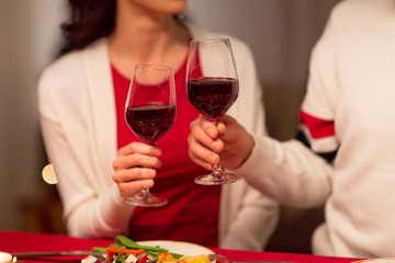 holidays, family and celebration concept - close up of happy couple having christmas dinner at home and drinking red wine