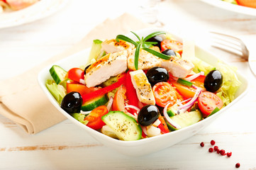 Chicken salad with cherry tomatoes, black olives, cucumber, red onion, red pepper, lettuce and fresh rosemary. Home made food Concept for a tasty and healthy meal Bright wooden background. Copy space 