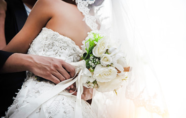 Naklejka premium The wedding couple.Bride and groom holding together,with white rose bouquet in hand,blurry lightaround