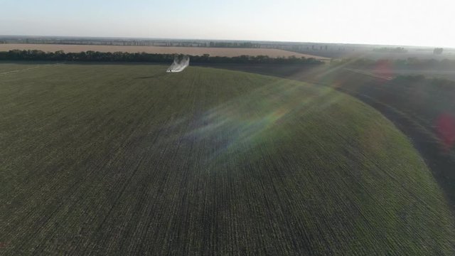 vintage propeller plane in sunny sky flies over green field with wheat and splashing chemicals against pests into agriculture in drone view