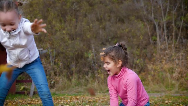 Two little girls throw autumn leaves. Child playing in autumn garden. Fall foliage. Outdoor fun in autumn. 4k 60fps slow motion.