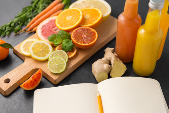 food, healthy eating and vegetarian concept - close up of citrus fruits on wooden cutting board, bottles of juices and notebook on slate table top