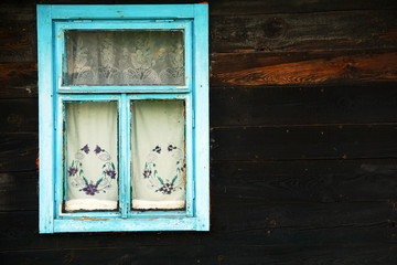 Window with blue frames and old curtains in a wooden old house, Belarus