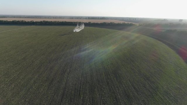 vintage beautiful Aircraft in sunlight flies over green field with wheat and does chemical treatment against pests into agricultural in drone view
