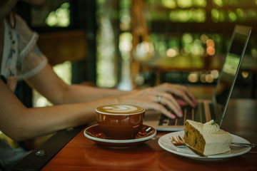 Top view. Womens hand . Freelance working space. Notebook with  cup of coffee and dessert on wooden table.