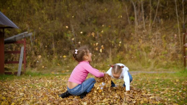Two little girls throw autumn leaves. Child playing in autumn garden. Fall foliage. Outdoor fun in autumn. 4k 60fps slow motion.