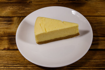 Piece of tasty sweet New York cheesecake in a white plate on wooden table