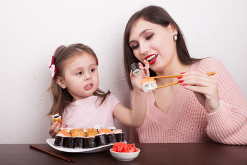 A girl is feeding her daughter a sushi of traditional Japanese food