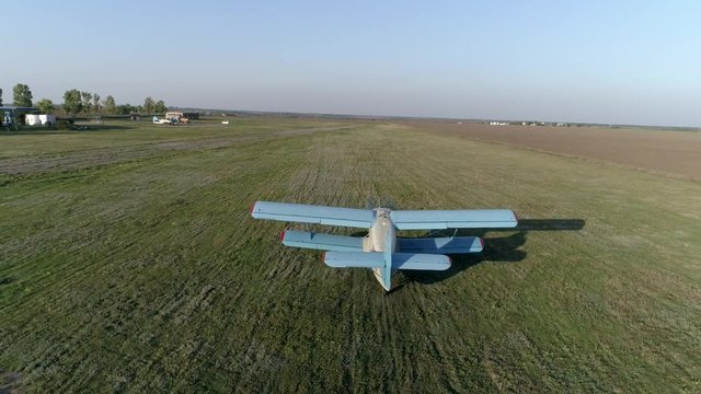 vintage propelled blue aircraft takes off over field against sky and horizon line in spring, drone view