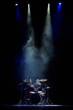 music, people, musical instruments and entertainment concept - male musician with drumsticks playing drums on the stage.