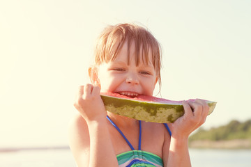 Little girl eating watermelon on the beach