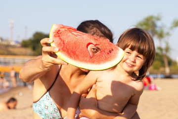 Little girl and her mother eating watermelon on the beach