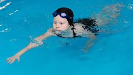 swimming lessons for children in the pool - beautiful fair-skinned girl swims in the water