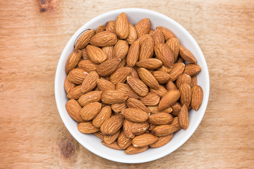 Almonds in a white cup rests on a wooden table