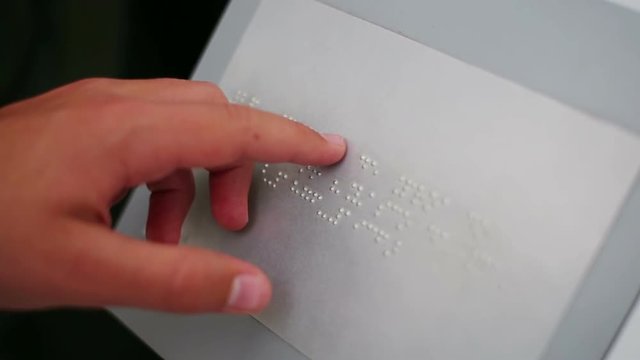 The hand of a blind man leads by the symbols of the alphabet Braille.