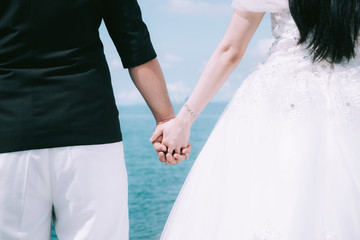 Adorable wedding couple holds each other hands walking along the beach against the  ocean waves in the evening light,groom and bride holding hands on beach