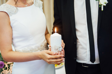 Candle in the hands of the newlyweds symbolizes hearth and well-being of the family