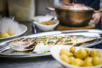 Freshly barbecued golden fish on silver tray with baked potatoes