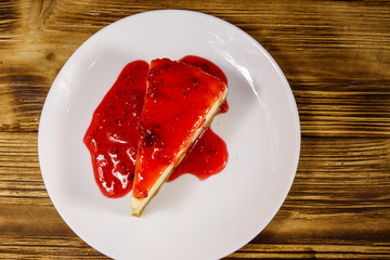 Piece of tasty New York cheesecake with raspberry jam in a white plate on wooden table. Top view