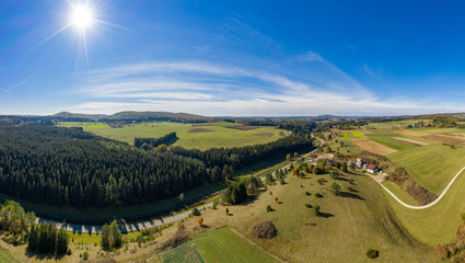 Fototapeta na wymiar Herbstliches Panorama mit einem Wald, einer Straße und der strahlenden Sonne am blauen Himmel