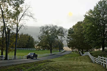 pickup truck on beautiful country road long fence green trees lawn © kentannenbaum46