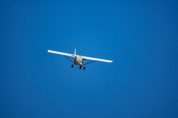 Fototapeta na wymiar Light aircraft flying over blue sky background
