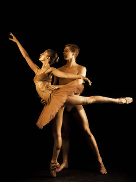 Professional, emotional ballet dancers on dark scene performed by sexual couple with golden body art.Shining gold skin.Pair depicts love and passion on stage