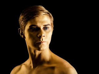 Close up portrait of handsome young ballet dancer with shining golden skin on black background. Body art with gold paint. Fashion style. Man model portrait