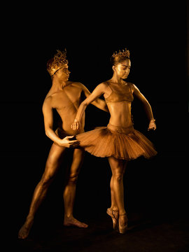 Professional, emotional ballet dancers with crowns on dark smoke scene performed by sexual couple king and queen with golden body art. Shining gold skin