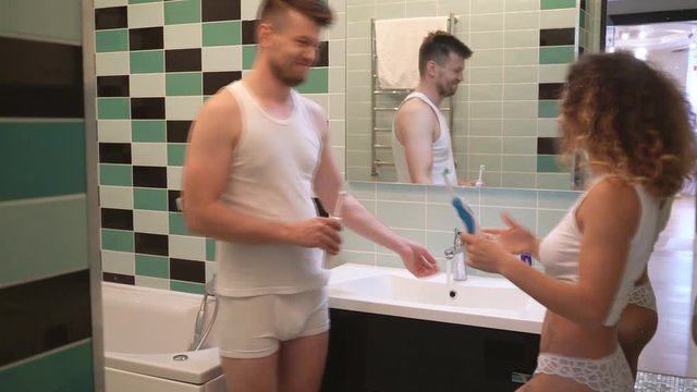 Happy girl 25 years old is splashing water in guy. Lovers indulge in the bathroom in front of the mirror. drops of water fly to the man's face 4к