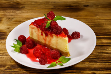 Piece of tasty New York cheesecake with raspberries and raspberry jam in a white plate on wooden table