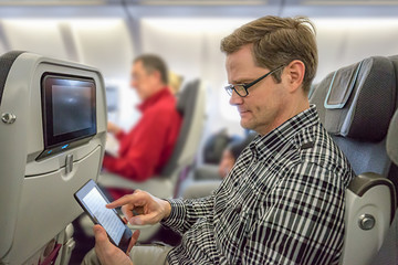 Mann sitzt entspannt im Flugzeug und liest ein eBook
