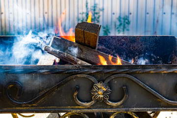 Plakat Metal grill, forged, handmade, with a pattern. A hot fire on the wood with smoke for barbecue and grilled products. Outside on a Sunny day.