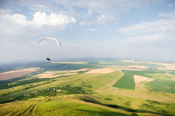 A white-orange paraglider flies over the mountainous terrain