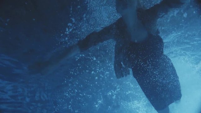 Amazing woman in a black dress swimming in the night time on the pool some moonlight falls into the water.