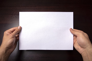 A clean white sheet in the hands is located horizontally on a dark background.