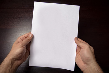 A clean white sheet in the hands is located vertically on a dark background.