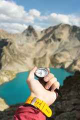 A man's hand holds a pocket magnetic compass for navigation against the backdrop of a rocky slope and a mountain lake. The concept of finding a way. Gaining freedom. freedom of choice