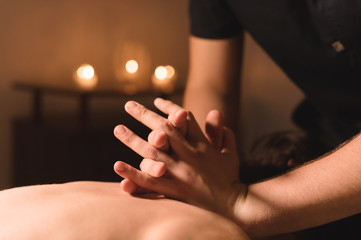 Men's hands make a therapeutic neck massage for a girl lying on a massage couch in a massage spa with dark lighting. Close-up. Dark Key