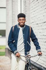 Fototapeta na wymiar african american stylish man with bike standing near white brick wall