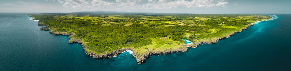 Panorama island, ocean. Aerial drone shot. Indonesia. Spectacular overview of Sumba island the green-capped plain surrounded by the Indian ocean on the blue cloudy sky background.