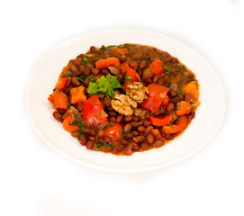 Plate of stewed beans with vegetables on white background