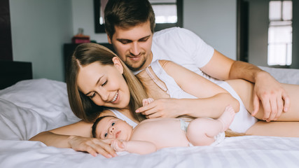 cheerful family laying with adorable little baby son in bed at home