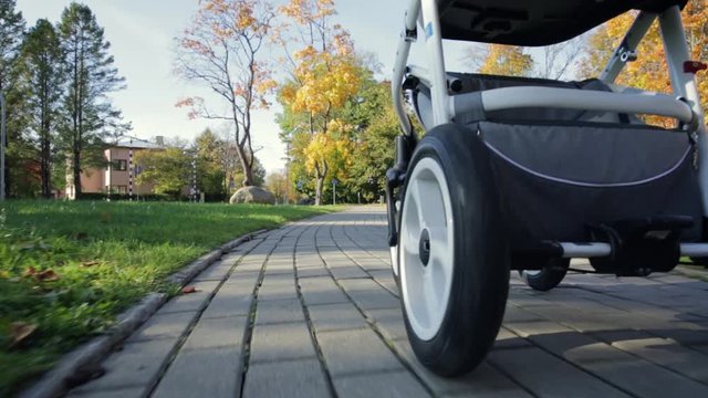 Close Up of baby strollers wheel. Women walking baby in park with colorful trees in autumn.