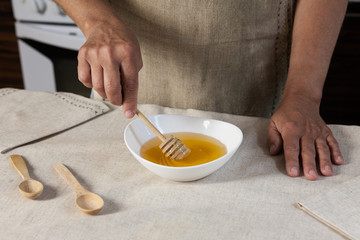 Woman's hand holding honey dipper above white bowl with honey.