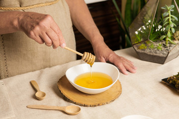 Obraz na płótnie Canvas Woman's hand holding honey dipper above white bowl with honey.